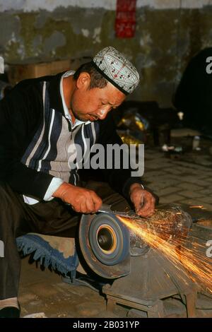 La piccola oasi dominata dagli uiguri di Yengisar (Yingjisha) è conosciuta in tutta la provincia cinese occidentale dello Xinjiang per la produzione di coltelli fatti a mano. La fabbrica di coltelli piccoli (Pichak Chilik Karakhana / Xiaochang) impiega abili artigiani locali che producono coltelli sottili con manici intarsiati. Appena circa ogni uomo di Uighur porta un coltello, sia come segno di manhood che per lo scopo più utilitaristico di tagliare i meloni ed il più stimato (e costoso) viene da Yengisar. Foto Stock