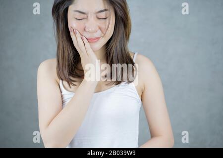 Dolore E Dentista Dei Denti. Giovane Donna Asiatica Che Soffre Di Terribile Forte Dolore Ai Denti, Toccando Guancia Con Mano. Foto Stock