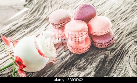 Amaretti rosa lampone e fragola con decorazioni in valentine pastello e fiori di rosa su sfondo morbido, DOF poco profondo. Delicati macaroni sul tavolo su Light ba Foto Stock