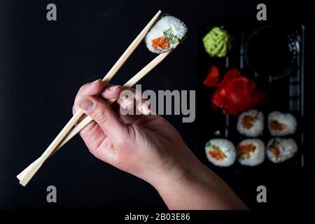 Maniglie con bastoni cinesi rotolo di sushi su sfondo nero. Set di sushi da portare con te con un rotolo. Foto Stock