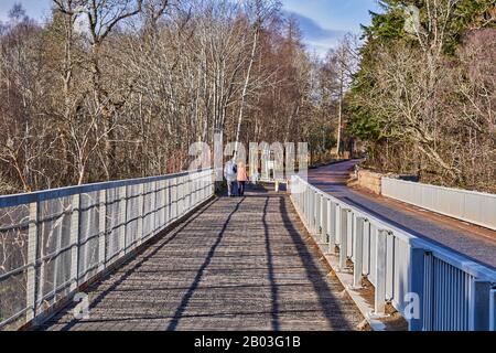 CARRON VILLAGE MORAY SCOZIA ESCURSIONISTI SULLA STRADA UNICA CARRON E VECCHIO PONTE FERROVIARIO CHE ATTRAVERSA IL FIUME SPEY Foto Stock