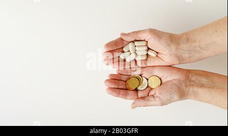 Donna anziana che detiene monete e pillole in euro nelle sue mani. Concetto di previdenza e problemi finanziari. Foto Stock