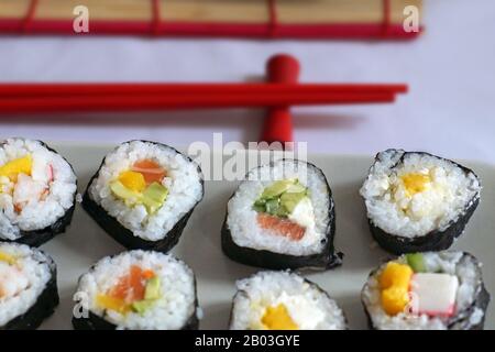 Tappetino e bacchette. Diversi tipi di sushi serviti su un piatto rettangolare. Foto Stock