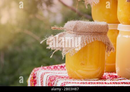 Vaso di vetro con miele avvolto nella materia è sul tavolo sotto un caldo sole di primavera con copyspace Foto Stock