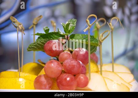 Bel piatto di frutta con ananas a fette, mela, menta e uva sfondo blu Foto Stock