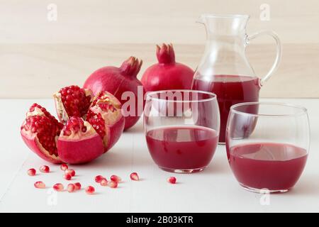 Caraffa e due bicchieri di succo di melograno fresco, con tre melograni maturi, uno appena sbucciato. Semi di melograno rossi in primo piano, tutti o Foto Stock