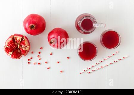 Caraffa e due bicchieri di succo di melograno fresco, con tre melograni maturi, uno appena sbucciato. Semi di melograno rossi in primo piano, tutti o Foto Stock