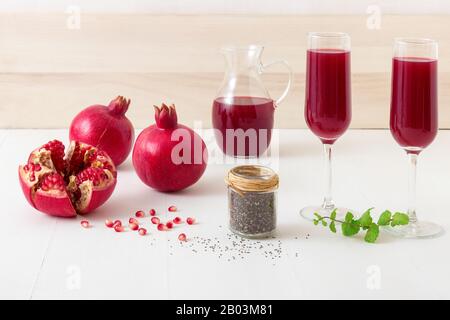 Melograni e semi di chia con menta fresca. Una caraffa in vetro di succo rosso fresco con due bicchieri pieni. Un'invitante bevanda fresca su un tavolo bianco pulito Foto Stock