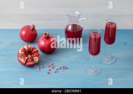 Caraffa e due bicchieri di succo di melograno fresco, con tre melograni maturi, uno appena sbucciato. Semi di melograno rossi in primo piano, tutti o Foto Stock