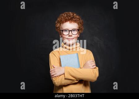 Ritratto di capretto della scuola in occhiali che tengono il libro Foto Stock