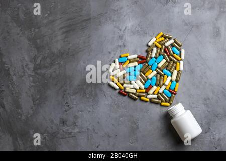 Flacone bianco e pillole multicolore a forma di cuore. Sfondo grigio in cemento. Concetto di farmaci, medicinali, farmaci per il trattamento di Foto Stock