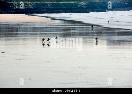 Surfers con tavole da surf specchiate e riflesse su sabbia bagnata a Fistral Beach, Newquay, la Cornish Coast, Inghilterra Foto Stock