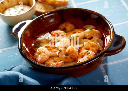 Ciotola di terracotta marrone con scampi grigliati speziati freschi o aragosta in una vista ad alto angolo su una superficie di piastrelle blu Foto Stock