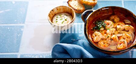 Ciotola di scampi mediterranei speziati freschi o aragosta servita con una salsa di vinaigrette sul lato su uno sfondo piastrellato blu e bianco con spazio copia i Foto Stock