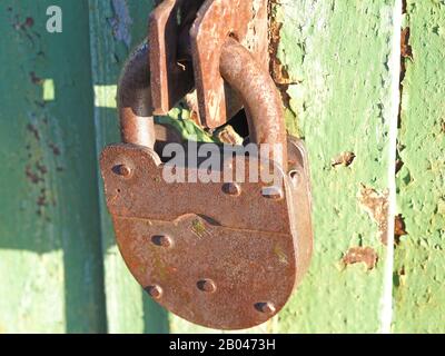 Un vecchio lucchetto arrugginito pende su una porta metallica. Il concetto di protezione della proprietà Foto Stock