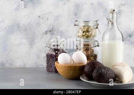 Cibo ricco di biotina. Fonti naturali di vitamina B7. Cibo : latte pollo uova noci fagioli avocado in vaso di vetro su sfondo blu copia spazio Foto Stock