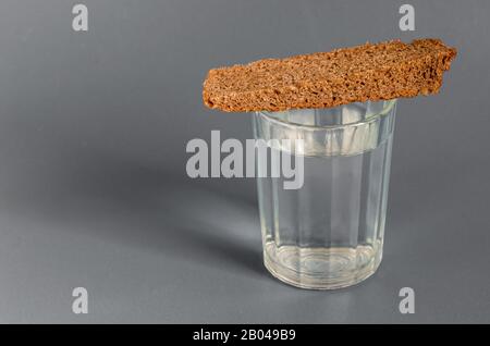 Bicchiere pieno sfaccettato di forte alcol e pane su sfondo grigio. Colori calmi. Primo piano. Messa a fuoco selettiva. Foto Stock