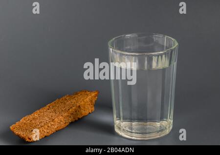 Vetro sfaccettato di forte alcol e pane su sfondo grigio. Colori calmi. Primo piano. Messa a fuoco selettiva. Foto Stock