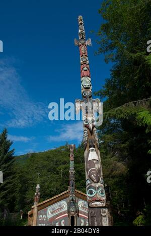 Tlingit totem pole con clan house in background al Totem Bight state Historical Park di Ketchikan, Alaska sud-orientale, Stati Uniti. Foto Stock