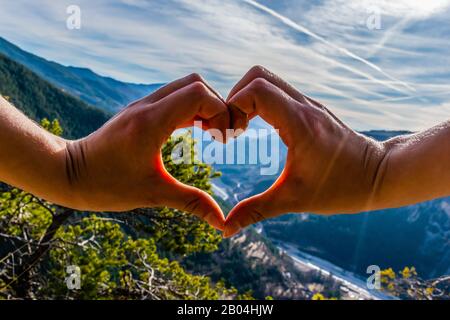 Natura amorevole: La stretta delle mani femminili a forma di cuore sullo sfondo della valle e della natura della montagna Foto Stock