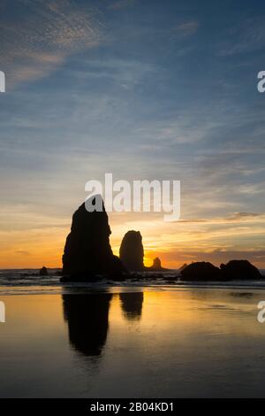 Le pile di mare si silhouette al tramonto durante la bassa marea a Cannon Beach sulla costa settentrionale dell'Oregon, Stati Uniti. Foto Stock