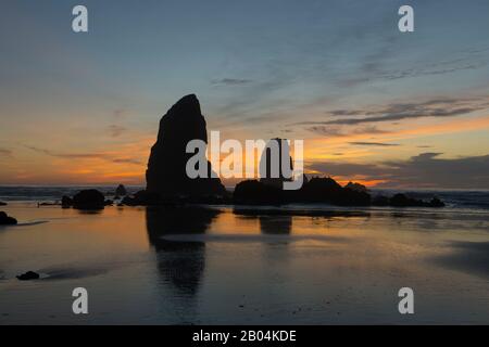 Le pile di mare si silhouette al tramonto durante la bassa marea a Cannon Beach sulla costa settentrionale dell'Oregon, Stati Uniti. Foto Stock