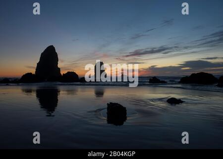 Le pile di mare si silhouette al tramonto durante la bassa marea a Cannon Beach sulla costa settentrionale dell'Oregon, Stati Uniti. Foto Stock