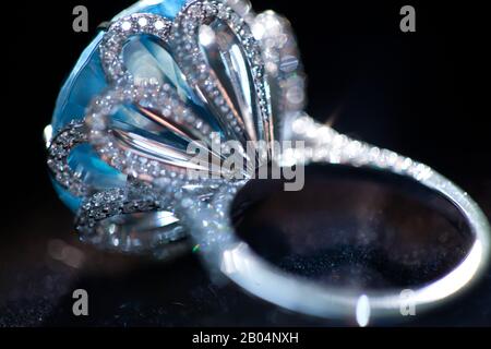 macro scatto di un anello bianco di metallo prezioso con grande gemma blu, su sfondo nero Foto Stock