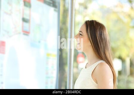 Vista laterale ritratto di un felice commuter controllo tabella di programmazione in attesa in una fermata di autobus Foto Stock