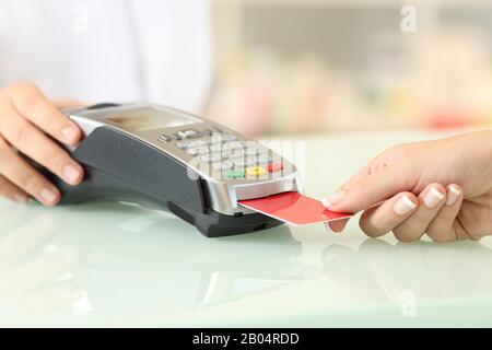 Primo piano di un cliente mani che pagano con lettore di carta di credito su un banco in una farmacia Foto Stock