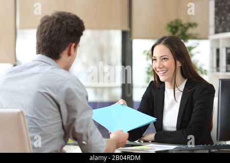 Dipendente che dà cartella al suo manager felice durante il colloquio in ufficio Foto Stock