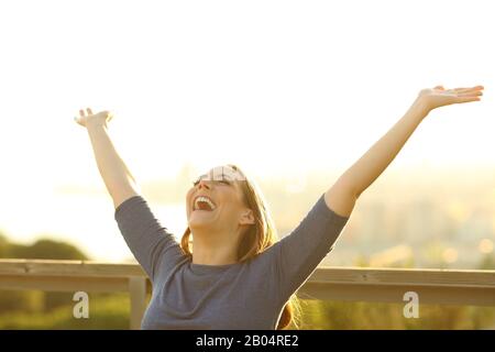 Donna felice seduta su una panchina che solleva le braccia celebrando la vita in un parco Foto Stock