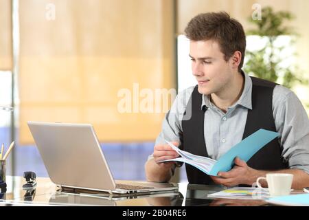 Lavoratore serio che confronta i contenuti online dei notebook e i documenti cartacei in ufficio Foto Stock