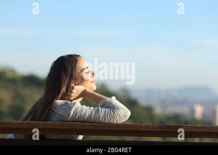 Vista laterale ritratto di donna rilassante sollievo stress seduta su una panchina nella periferia della città Foto Stock