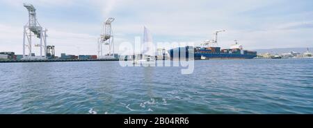 Barca a vela e container di fronte a un molo commerciale, Porto di Oakland, San Francisco, California, Stati Uniti Foto Stock