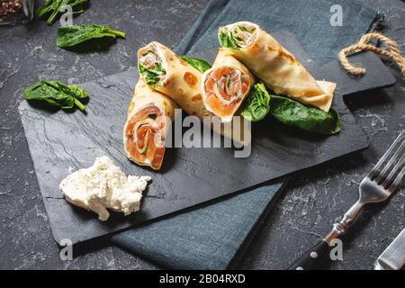 Deliziosa colazione o brunch - crepes con salmone affumicato, spinaci e panna acida su sfondo di pietra. Foto Stock