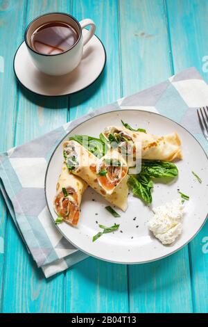 Deliziosa colazione o brunch - crepes con salmone affumicato, spinaci e panna acida su sfondo di legno blu. Foto Stock