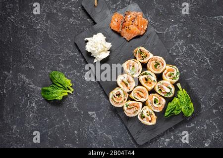 Involtini di frittelle piene di salmone affumicato, formaggio cremoso su sfondo di pietra nera. Vista dall'alto Foto Stock