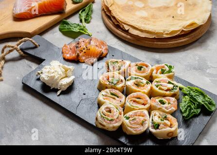 Involtini di frittelle ripiene di salmone affumicato, formaggio cremoso su fondo di cemento. Foto Stock