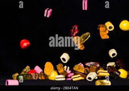 Molti dolci e colorati caramelle stanno cadendo giù ad un tavolo nero Foto Stock
