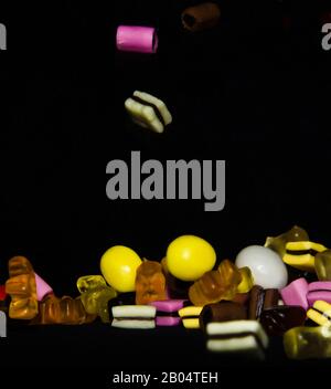 Molti dolci e colorati caramelle stanno cadendo giù ad un tavolo nero Foto Stock