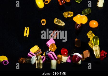 Molti dolci e colorati caramelle stanno cadendo giù ad un tavolo nero Foto Stock