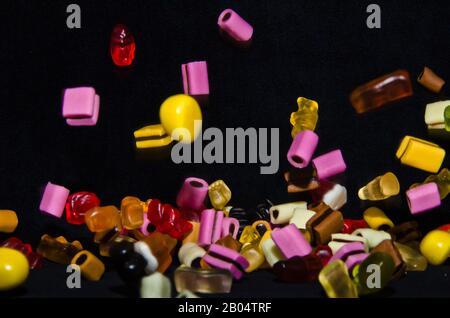 Molti dolci e colorati caramelle stanno cadendo giù ad un tavolo nero Foto Stock