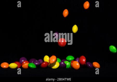Molti dolci e colorati caramelle stanno cadendo giù ad un tavolo nero Foto Stock