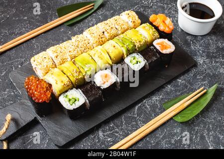 Vari tipi di sushi servita sulla pietra nera dello sfondo. Foto Stock