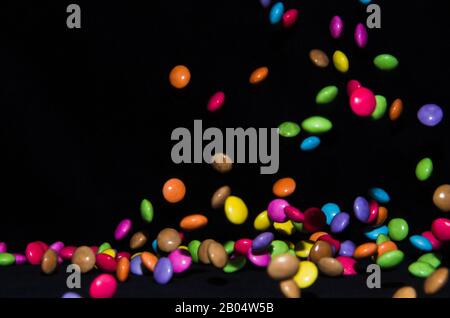Molti dolci e colorati caramelle stanno cadendo giù ad un tavolo nero Foto Stock