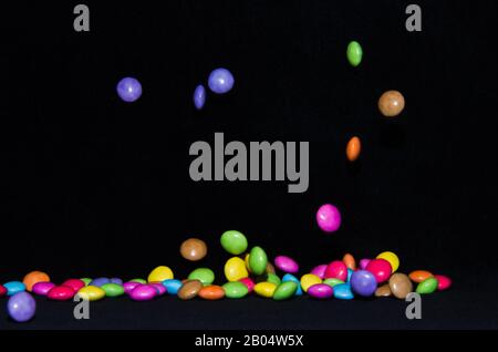 Molti dolci e colorati caramelle stanno cadendo giù ad un tavolo nero Foto Stock