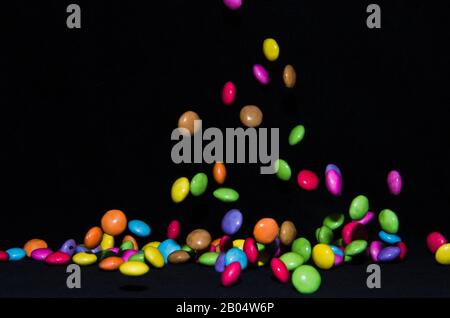 Molti dolci e colorati caramelle stanno cadendo giù ad un tavolo nero Foto Stock