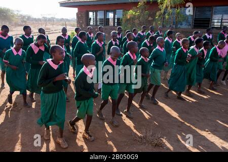 I bambini della scuola che danzano durante l'assemblea al mattino nel cortile di una scuola per i bambini Masai fuori del Parco Nazionale di Amboseli Foto Stock