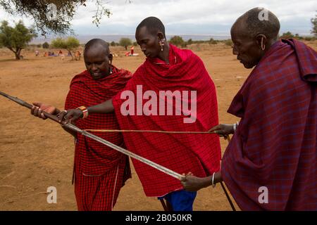 Scena del villaggio con uomini Masai che guardano una lancia tradizionale in un villaggio Masai fuori del Parco Nazionale Amboseli in Kenya. Foto Stock